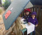 2 children playing shop in a cubby house outside