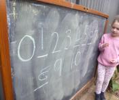 Child standing next to a large chalk board with numbers 0 to 10