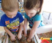 Two children playing with colourful sand and digging