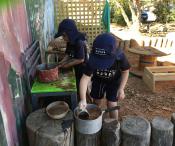 Children mixing mud in pots and pans in the playground kitchen