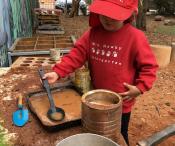 A child making a cake out of mud, in the kitchen area of the playground. 