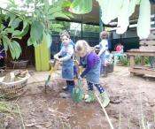 Children outside in gumboots and aprons playing with spades in a mud patch