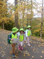 3 children in hi-vis jackets walking on a leafy littered road